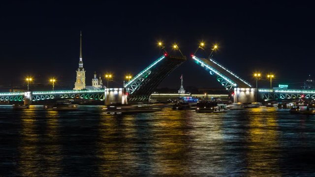 Night view on the Peter and Paul fortress and the Palace bridge lifting, boats floating along the Neva under the open bridge. Saint-Petersburg, Russia.