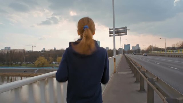 SlowMotion of Nice Young Lady in Sportswear Running on a Bridge in the City. Female jogging back view