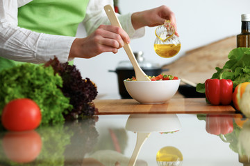 Closeup of human hands cooking vegetables salad in kitchen on the glass table with reflection. Healthy meal and vegetarian concept