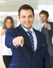 Happy smiling businessman and his colleagues pointing by finger into the camera. Concept of employer and success team.