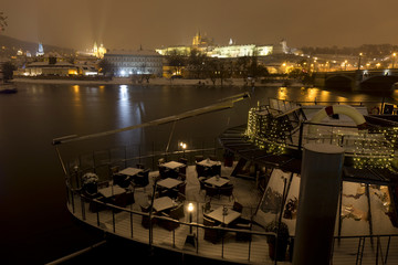 Night snowy Prague Lesser Town with gothic Castle above River Vltave, Czech republic