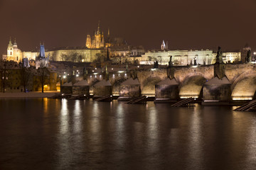 Fototapeta na wymiar Night snowy Prague Lesser Town with gothic Castle, St. Nicholas' Cathedral and Charles Bridge, Czech republic
