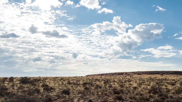 A scenic daytime drive time lapse on a gravel road with two dirt tracks in a grassy landscape setting with a blue sky and scattered clouds, side point of view 