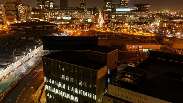 Night timelapse shooting down between buildings onto a street with peak traffic, buildings and a taxi rank in the city centre of Johannesburg, South Africa