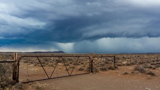 A static timelapse shot of a typical Karoo farm landscape with an old rusted gate and fence while an intense storm is approaching with dark and stormy skies or supercell clouds, South Africa