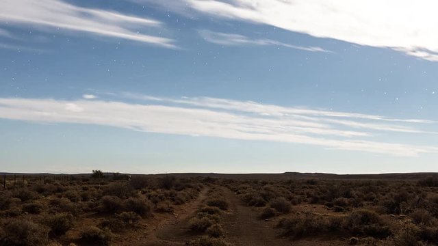 A slow push-in linear timelapse of a moonlit farm landscape in the Karoo with fast moving fleece clouds and a starry sky as the moon sets with a focus pull to blur