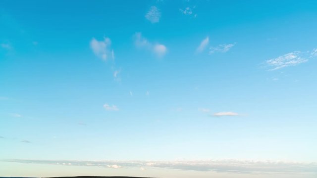 An early morning timelapse slowly tilting down onto vast open plains with a few scattered clouds against a bright blue sky as the sun lights up the landscape