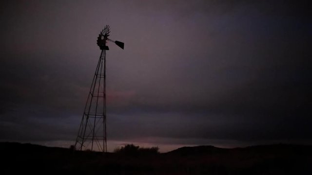 Static timelapse of a franticly blowing windmill silhouetted against a dramatic and stormy sky with clouds, thunder and lightning, clearing up later in the shot available on request.