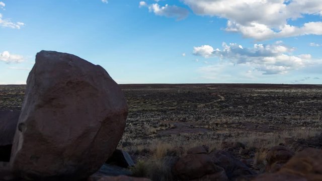 A static timelapse of a rocky Karoo farm landscape with a winding road and windmill in the distance, very fast moving clouds before sunset to twilight