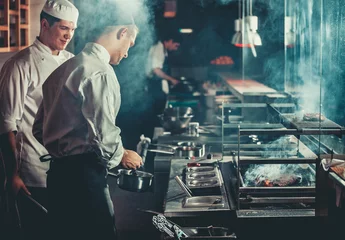 Foto op Aluminium Voedselconcept. Chef-kok in wit uniform bewaakt de mate van braden en smeert vlees met olie in pan in het interieur van de moderne restaurantkeuken. Voorbereiding van traditionele biefstuk op barbecue oven. © Goinyk