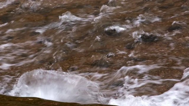 Zoomed view of water hitting rocks as it flows down stream.