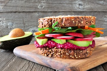 Superfood sandwich with beet hummus, avocado, vegetables and greens, on whole grain bread against a...