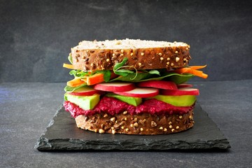 Superfoodsandwich met bietenhummus, avocado, groenten en greens, op volkorenbrood tegen een leisteenachtergrond