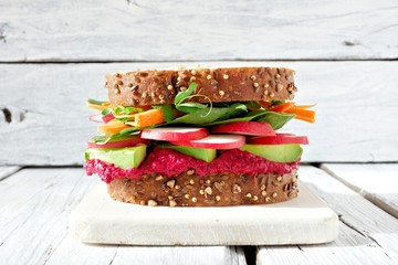 Superfood sandwich with beet hummus, avocado, vegetables and greens, on whole grain bread against a white wood background