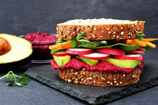 Superfood sandwich with beet hummus, avocado, vegetables and greens, on whole grain bread against a slate background