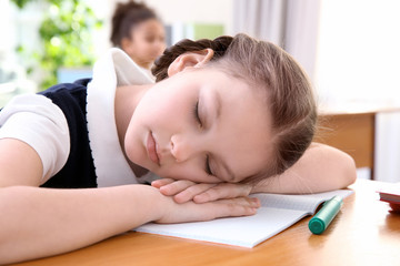 Obraz na płótnie Canvas Portrait of tired elementary schoolgirl sleeping on desk in classroom