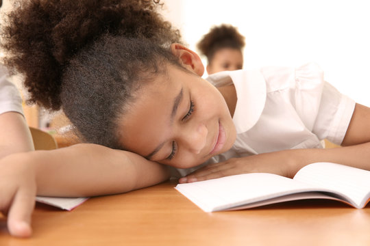 Portrait of tired elementary schoolgirl sleeping on desk in classroom