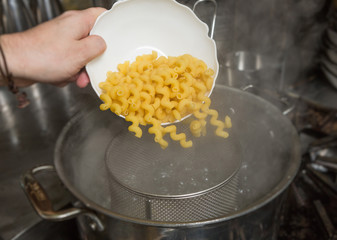 Dropping uncooked Macaroni pasta into a steaming hot pan of water.