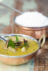 A delicious spicy prawn green curry, served with sticky rice in a rustic metal pan.