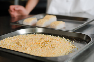 Fresh fish fillet cube covered in breadcrumbs, being placed onto a metal baking tray.