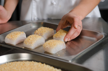 Fresh fish fillet cube covered in breadcrumbs, being placed onto a metal baking tray.