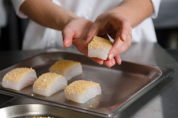 Fresh fish fillet cube covered in breadcrumbs, being placed onto a metal baking tray.