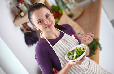 Young woman eating fresh salad in modern kitchen