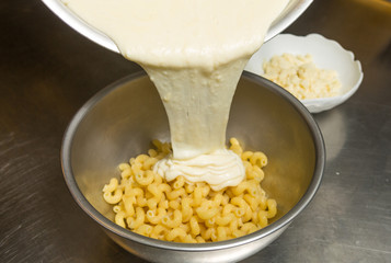 Melted cheese being poured onto cooked Macaroni pasta.