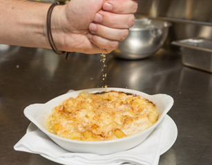 Cooked breadcrumbs being sprinkled onto oven bake macaroni cheese.
