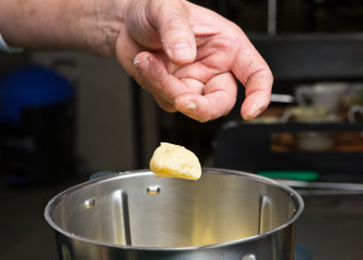 Close up shot of a hand dropping butter onto fluffy peeled potatoes in a blender.