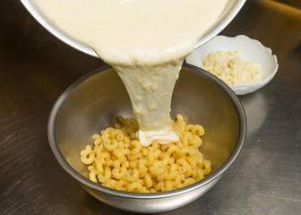 Melted cheese being poured onto cooked Macaroni pasta.