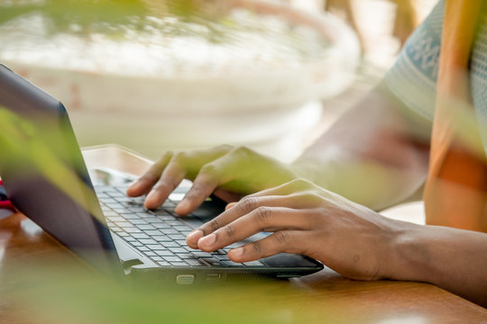 hands typing on laptop keyboard. Black person working with computer outdoors blurred background. Freelancer at work. Selective focus