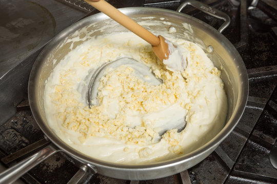 Cheese being mixed into a hot pan, to melt in preparation for Macaroni cheese