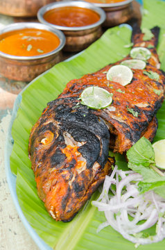 Grilled spicy fish tikka served with mint, lime, sauces and a banana leaf in a rustic setting.