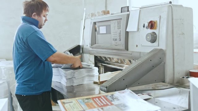 Man worker in blue t-shirt with cutter guillotine machine at printing factory - typography