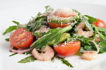 Obraz na płótnie Canvas salad of arugula leafs, cherry tomatoes, prawns, avocado, and red onion dressed with olive oil and balsamic vinegar sprinkled with grated parmesan