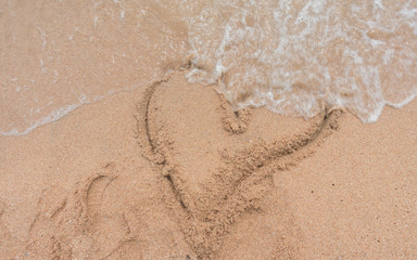 Little boy drawing sand by hand heart shape