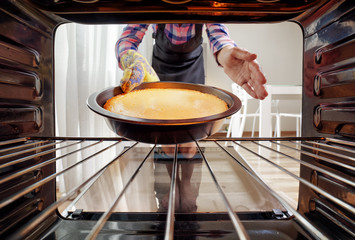 Woman taking cheesecake out of oven in kitchen