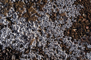 Close-up frozen water in lake with pebbles stone texture backgrounds