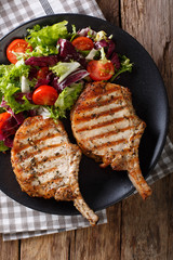 Barbecue spicy pork chop with fresh vegetable salad close-up. Vertical top view