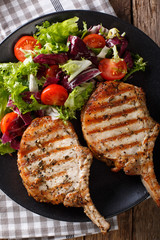 Grilled pork steak with bone, fresh vegetable salad close-up. Vertical top view