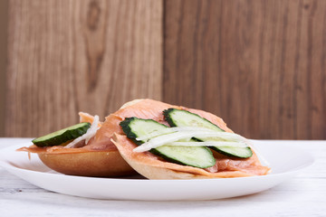 Bagel with salmon, cucumber, onion on white plate. Front view.