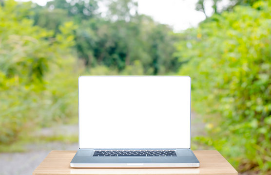 laptop with blank screen on wooden table outdoors and garden blurred background. Concept Online, freelancer working, communication , technology , shopping, banking