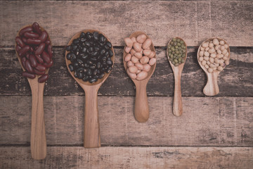 Bean seeds in wooden spoon on vintage style wooden background.