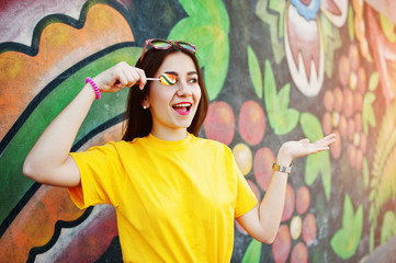 Beautiful teenage with lollipop, wear yellow t-shirt near graffiti wall.
