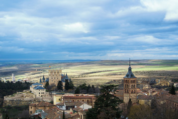 Fototapeta na wymiar Castle of Segovia, a tower and old medieval buildings with fields at the baackground, a view from an observation deck at Cathedral of the city, Castilla and Leon, Spain.