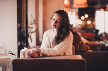 Stylish girl 24-29 year old sitting in restaurant wearing fluffy white sweater. 20s.