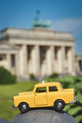 A yellow toy of a trabant taxi placed in front of the Brandenburg Gate in Berlin