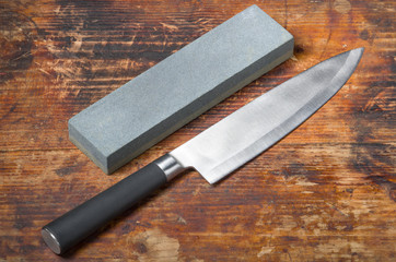 Knife and whetstone on  the old wooden cutting board