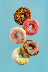 Various decorated doughnuts in motion falling on blue background.